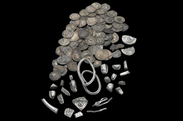 Pile of several dozen silver coins and various small silver fragments laid on a black surface.