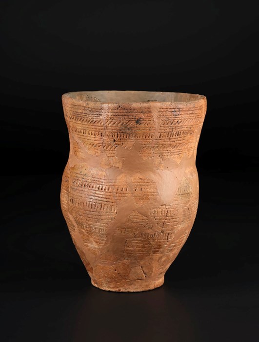 Reddish-brown Beaker vessel without lid, upright against a black background. Rows of vertical lines alternate with horizontal stripes.