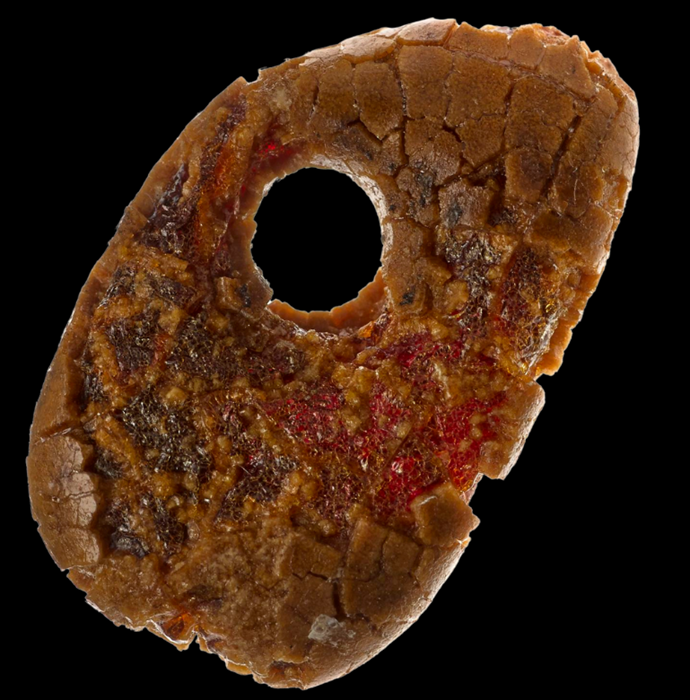 Bead shaped like a keychain fob. Reddish material that looks almost gum-like peaks out under a hard, cracked red-brown surface.