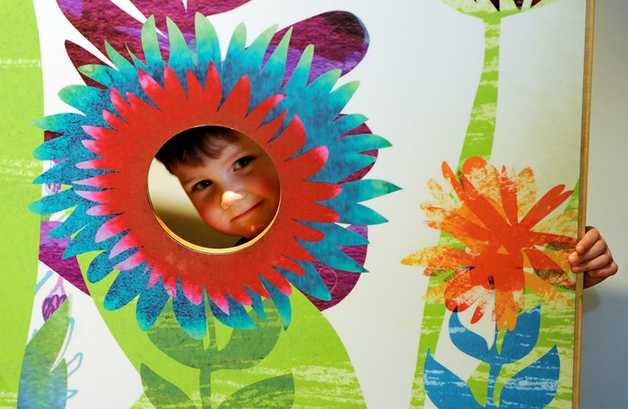 A young child popping their head through a hole that is surrounded with painted flower petals.