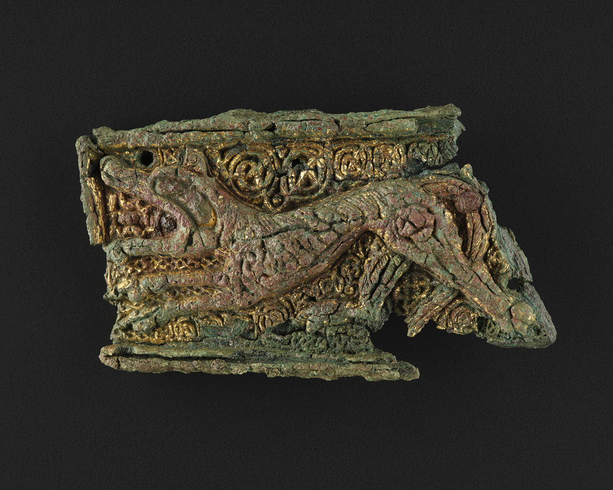 Rectangular bronze mount with cast decoration within a raised border of a wolf in high relief, with background of scrolls in low relief, from a grave of a woman and infant, Westness, Orkney, 850 - 900 AD