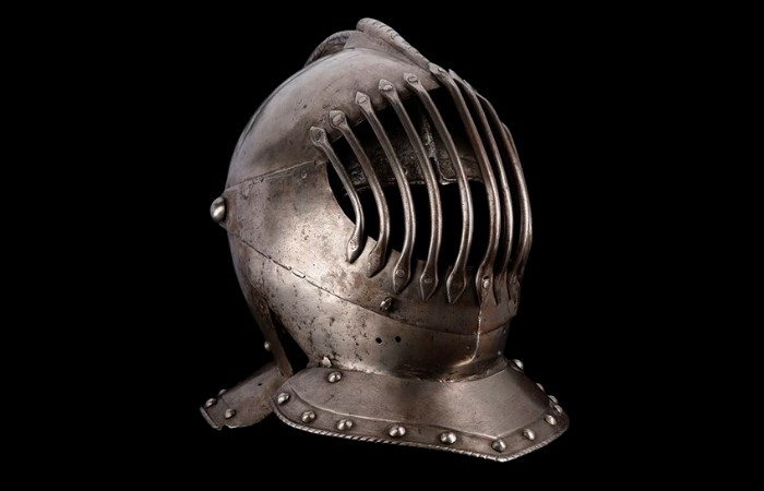 Sturdy steel helm with cage-like bars over the face, rivets around the neck and a small fin at the top.