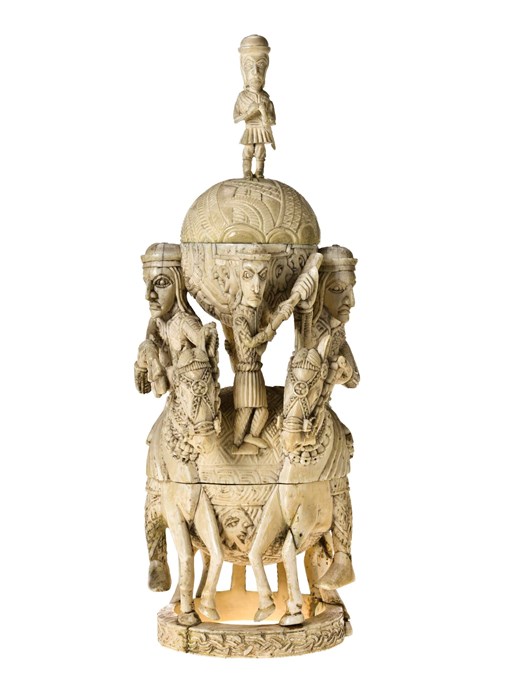 Tall, intricate ivory sculpture. Two men on horseback flack two large orbs. A small person stands on the bottom orb, another stands  on the top orb.
