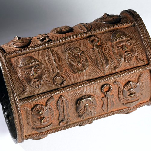 Brown-orange bronze armlet, shaped like a tube, decorated with bold symbols in relief.