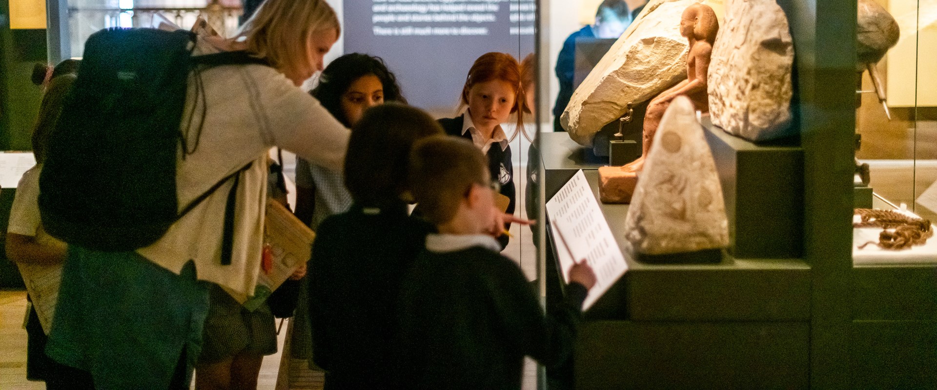 A teacher gathers a group of primary pupils around one of the cases in the Ancient Egypt Gallery. 