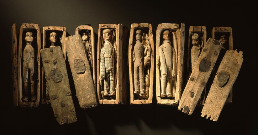 8 miniature wooden coffins with lids removed, revealing small figures inside.