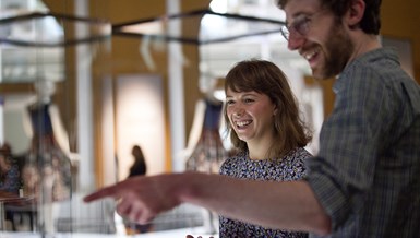 Woman and man smiling in a gallery with glass cases out of focus..