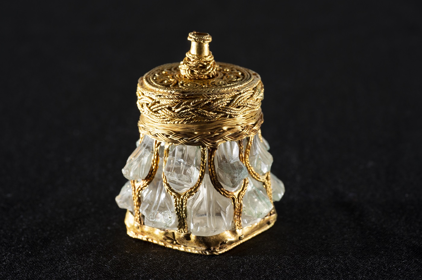 A small jar of light green crystal and shining gold stands upright against a black background.
