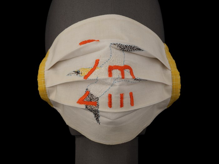 Face mask of white cotton embroidered with the image of a gannet in flight and ‘2m’, made by artist and designer Deirdre Nelson. X.2021.27.