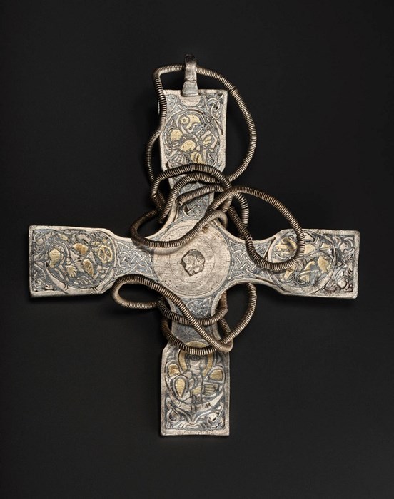 Silver cross with gold details on arms and a coil chain wrapped around its centre against a black background.