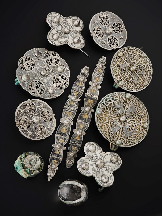 Group of 10 objects including circular brooches, two spheres and two belt-like fastenings against a black background.