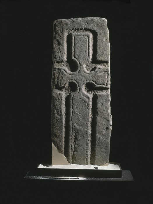 Tall rectangular stone slab with a deeply incised cross carved into it, taking up most of its surface.
