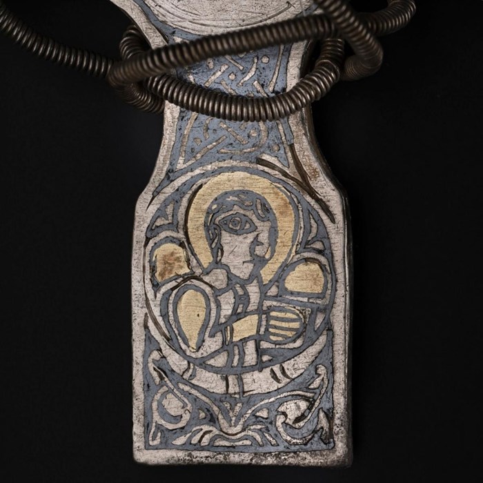 Closeup of lower arm of the cross. A saintly figure outlined in black draws the eye, sporting a golden halo and surrounded by naturalistic patterns.