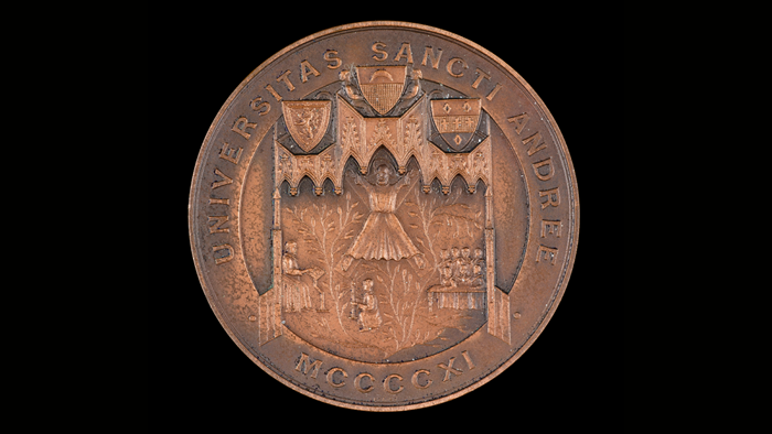 Bronze medal, faded with age, with a medieval scene in the centre, coats of arms, and 'Universitas sancti andree MCCCCXI' written around it.