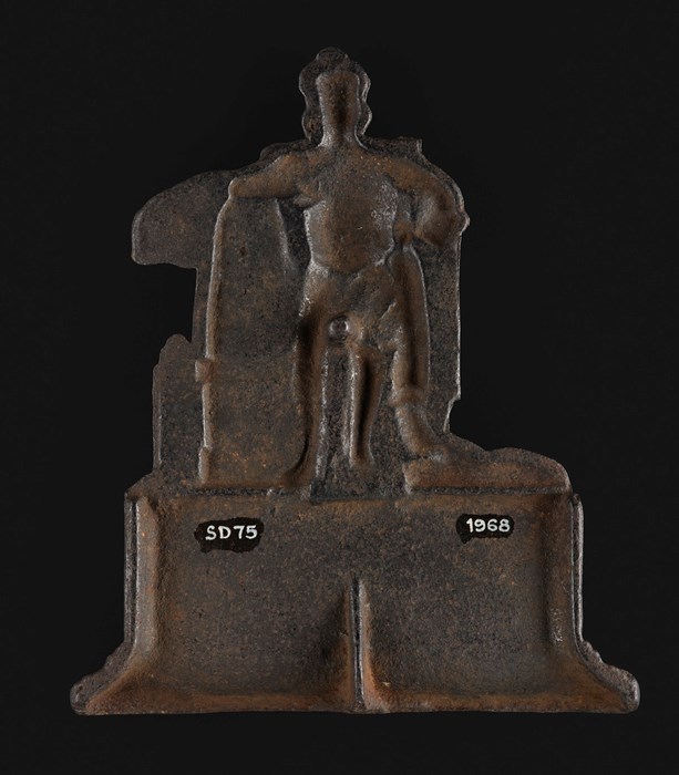 Reverse of a metal fireside ornament. Concave impression of a standing figure, otherwise blank.