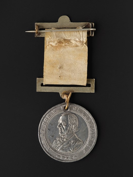 Circular silver medal engraved with the bust of an elderly statesman, attached to a faded yellow ribbon.