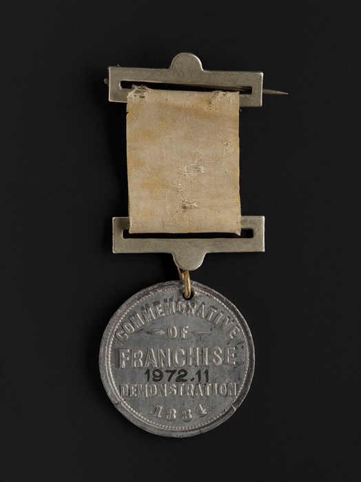 Circular silver medal engraved with 'Commemorative of Franchise Demonstration 1884', attached to a faded yellow ribbon.