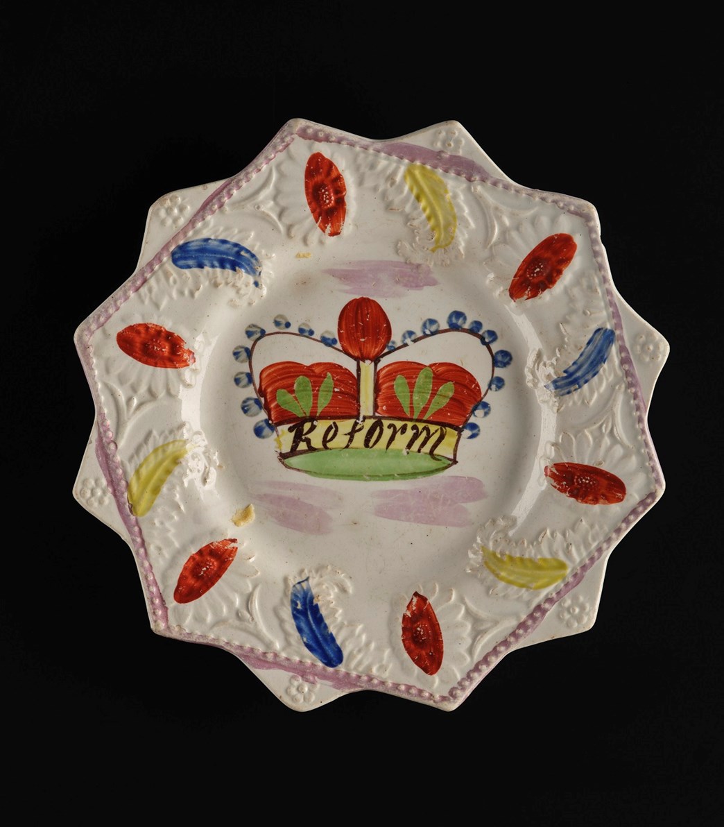 Plate shaped as a 12-pointed star. A red crown in the centre labelled 'Reform' surrounded by red, yellow and blue splotches.