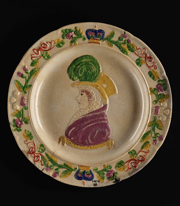 Off-white plate with a woman in a purple dress and yellow hat with green feathers facing sideways. bordered by crowns and flowers.