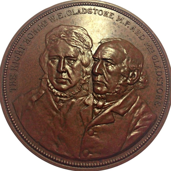 Round medal the colour of a penny with an elderly couple side by side. Mrs Gladstone on left, Mr Gladstone on right.