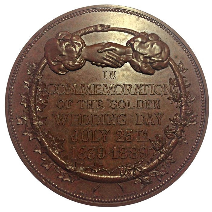 Round medal the colour of a penny with two clasped hands at the top, a wreath as a border, and text commemorating their wedding.