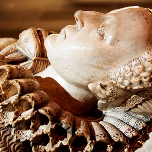 Closeup of a white stone tomb carved to depict Mary, Queen of Scots lying down in full dress.