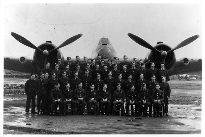 Four rows of aircraft crew posing for a photo in front of a large aircraft.