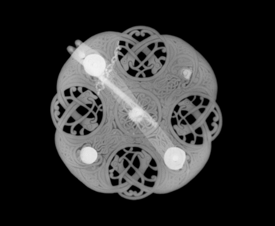 X-ray image of a circular brooch with with bold white bar diagonally across it and four circular areas with beast heads.