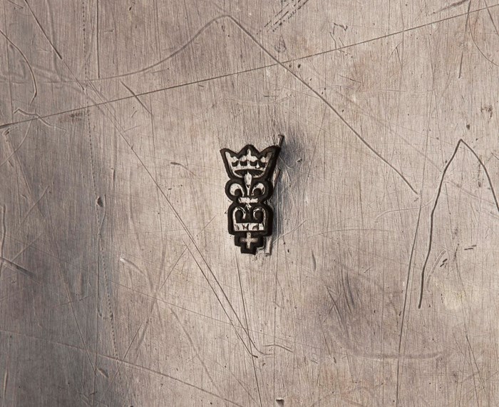 Extreme closeup of a maker's mark on a silver surface. A crown atop a fleur-de-lis atop another crown and a cross.