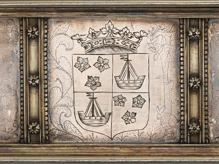 Coat of arms on a silver surface. A galley ship occupies the bottom left and top right sections, and three flowers occupy the bottom right and top left. A crown sits above all.