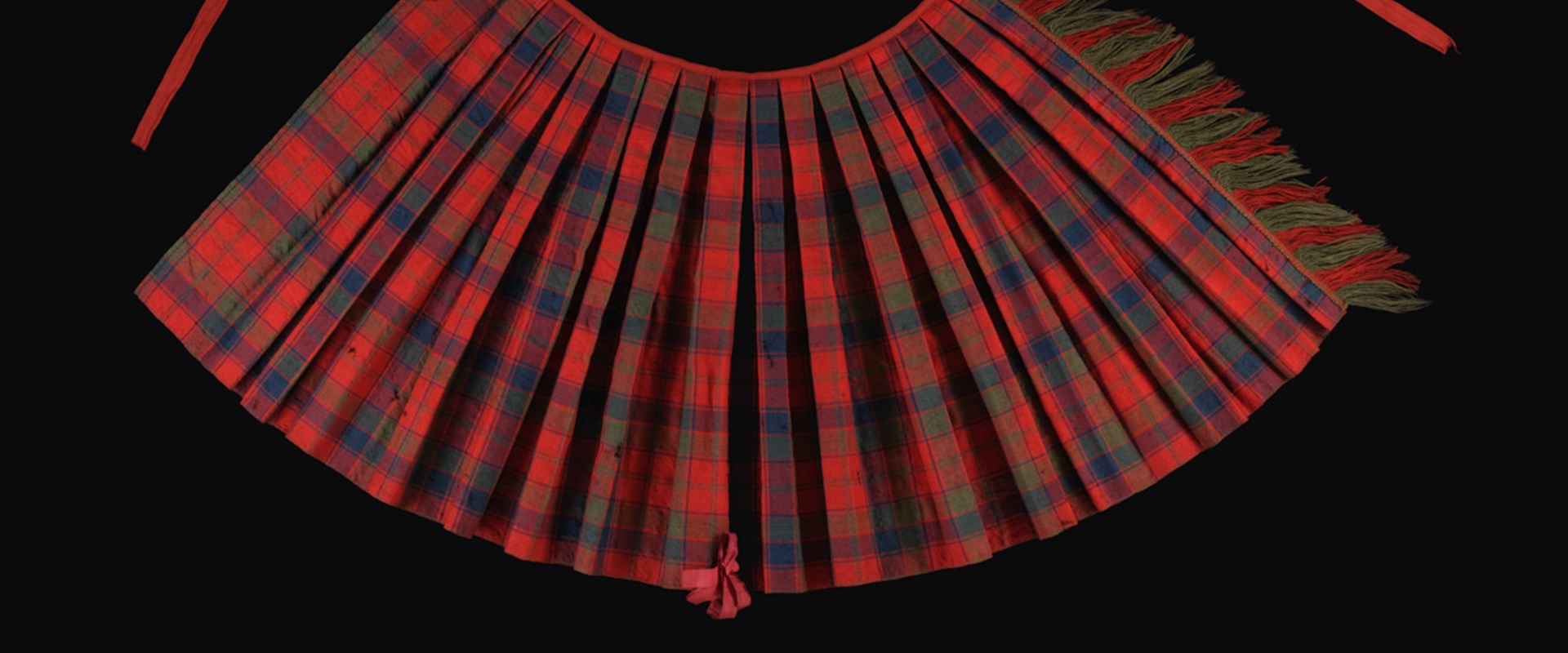 Pleated arc of red and green checkered tartan with strands at both top corners against a black background.
