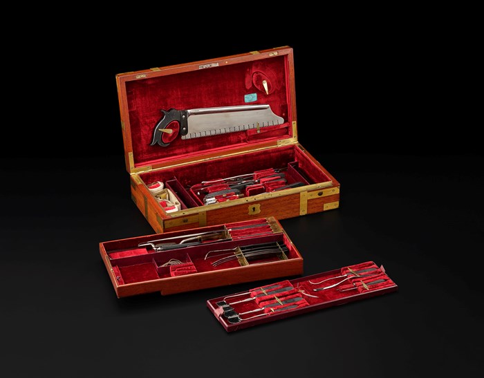 A red velvet lined, wooden box with tray inserts and various surgical tools.