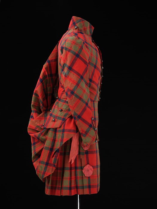 Resplendent bright red tartan suit viewed in profile facing right against black background. Very trim, accessorised and formal.