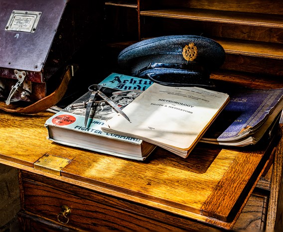 Pilot's books and an RAF cap on a wooden desk.