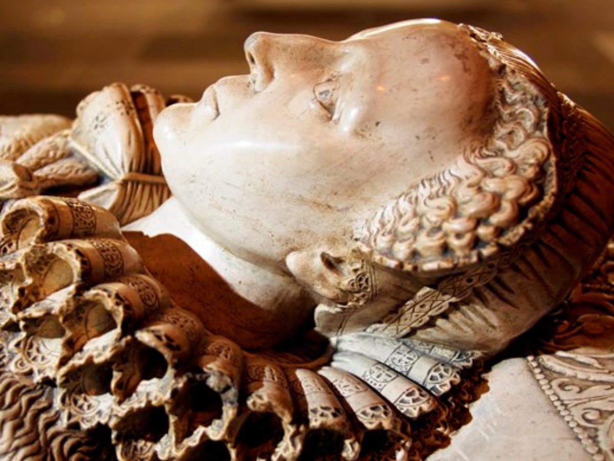 Closeup of the face of Mary, Queen of Scots depicted on a replica tomb viewed in profile. Frills ring her neckline. Her expression is stoic.