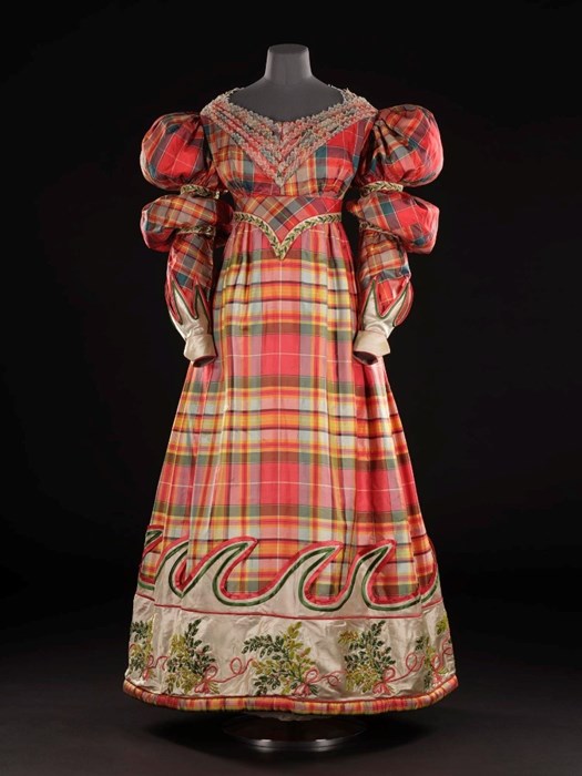 Very colourful red, yellow and green tartan dress with wave pattern at bottom. Exaggerated puffy arms and lace embroidery around neck.
