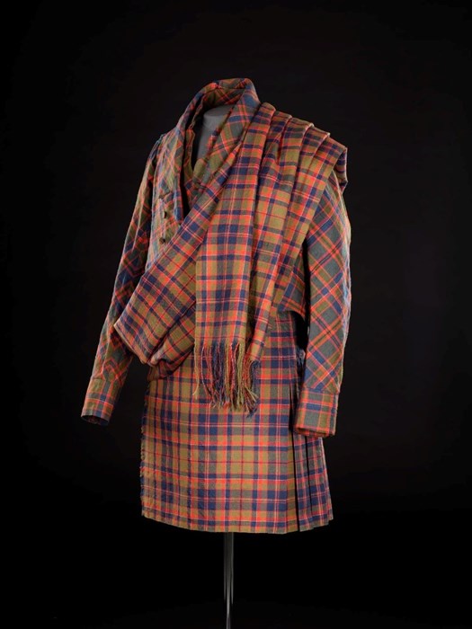 Tartan suit with short kilt on a mannequin against a black background. Tartan is yellow-green, blue and red. Looks modern and tailored.