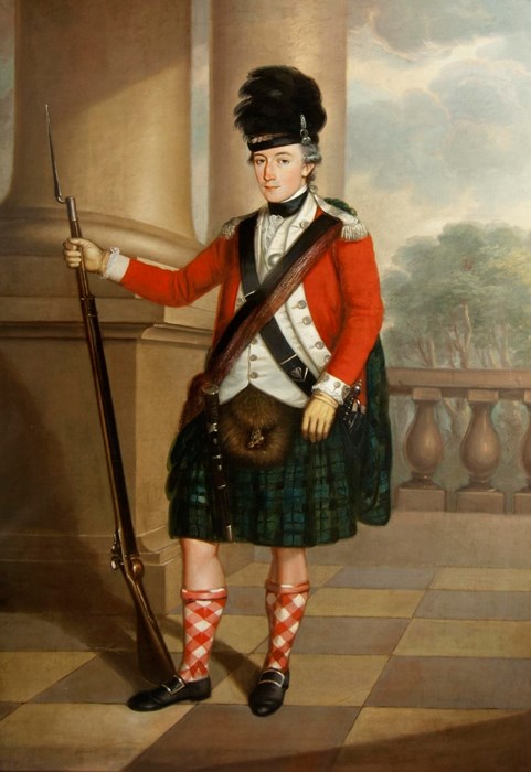 Soldier in red coat and green tartan kilt holds a rifle with bayonet on a balcony with two thick pillars behind him.