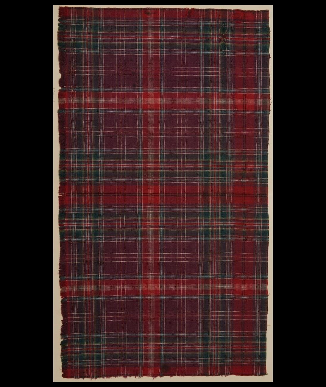Tall rectangular swatch of burgundy, dark blue, red and light green tartan fabric against a black background.