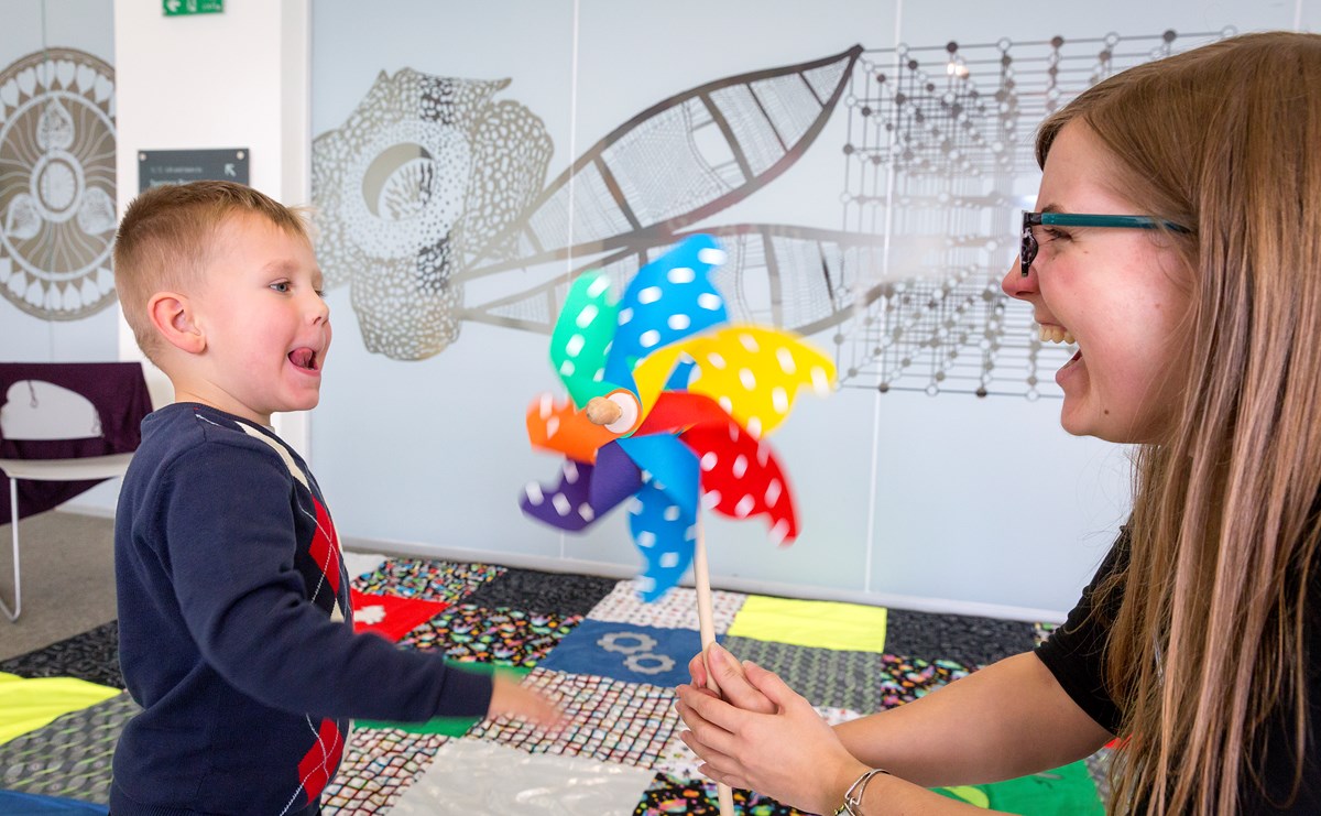 A learning enabler shows a small child a colourful windmill. They are both laughing