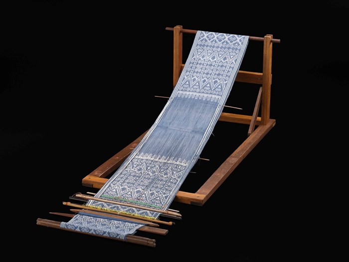 Length of silky blue and white cloth stretched over a wooden rack so as to resemble a beach folding chair.