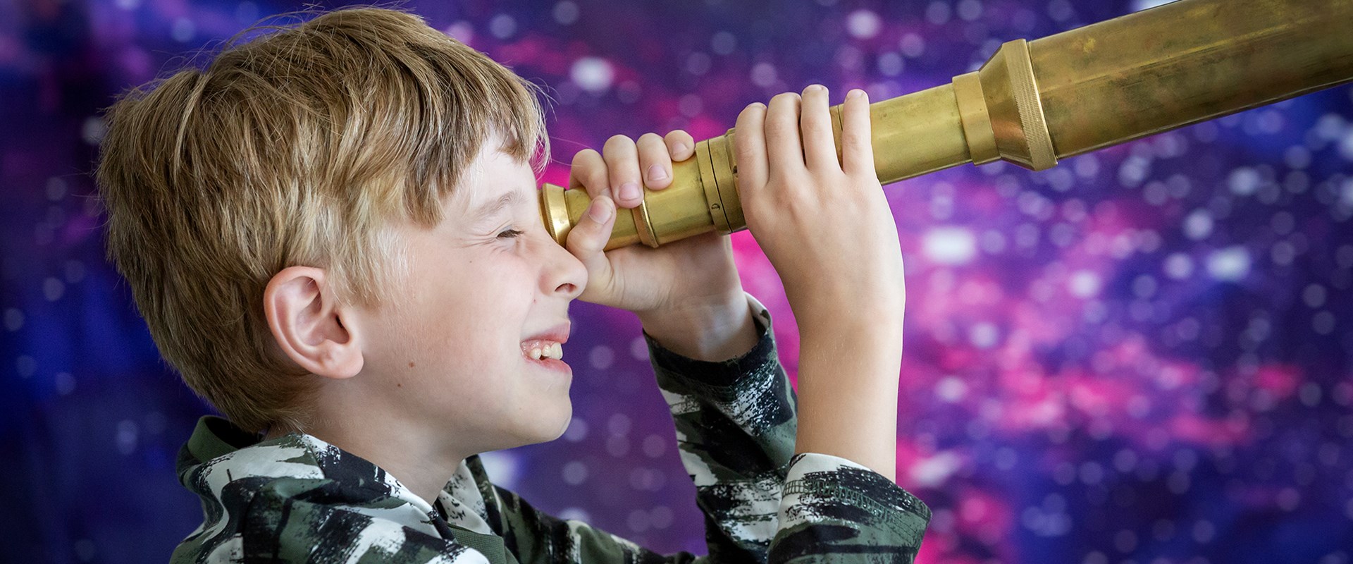 Child looks towards the right through a brass telescope.