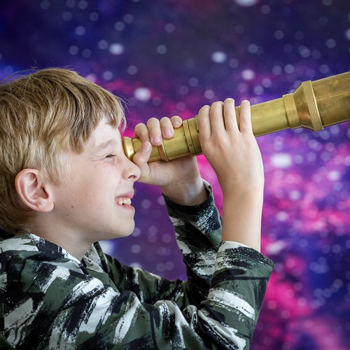 Child looks towards the right through a brass telescope.