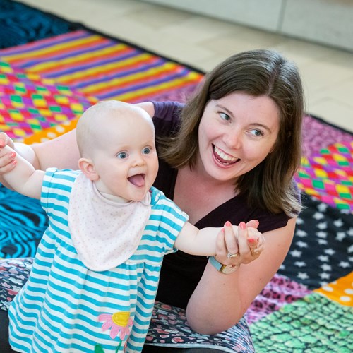 Woman and baby in arms sitting on the floor on a checked carpet.