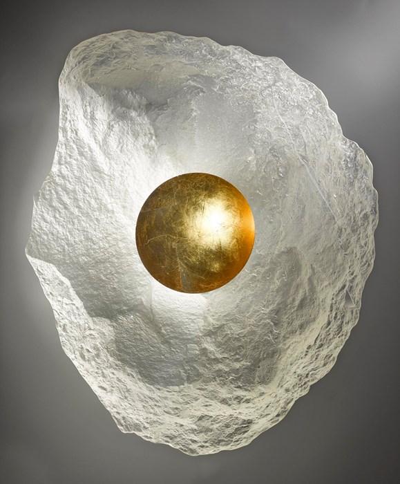 Sculpture of a natural-looking block of translucent white stone or crystal, with a radiant golden orb embedded in its centre.