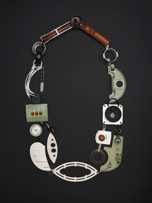 Large, blocky necklace made from the silver, light green and brown components of a coffee machine. Very robotic in its aesthetic.