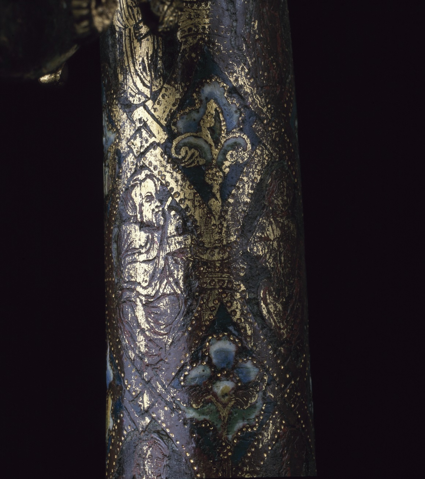 Closeup of the grey-blue crozier staff, revealing golden patterns of fleur-de-lis, flowers, and a saint.