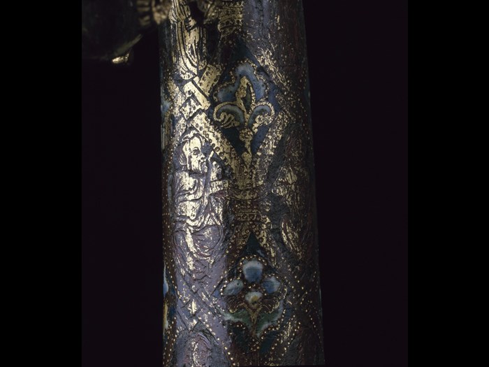 Closeup of the grey-blue crozier staff, revealing golden patterns of fleur-de-lis, flowers, and a saint.