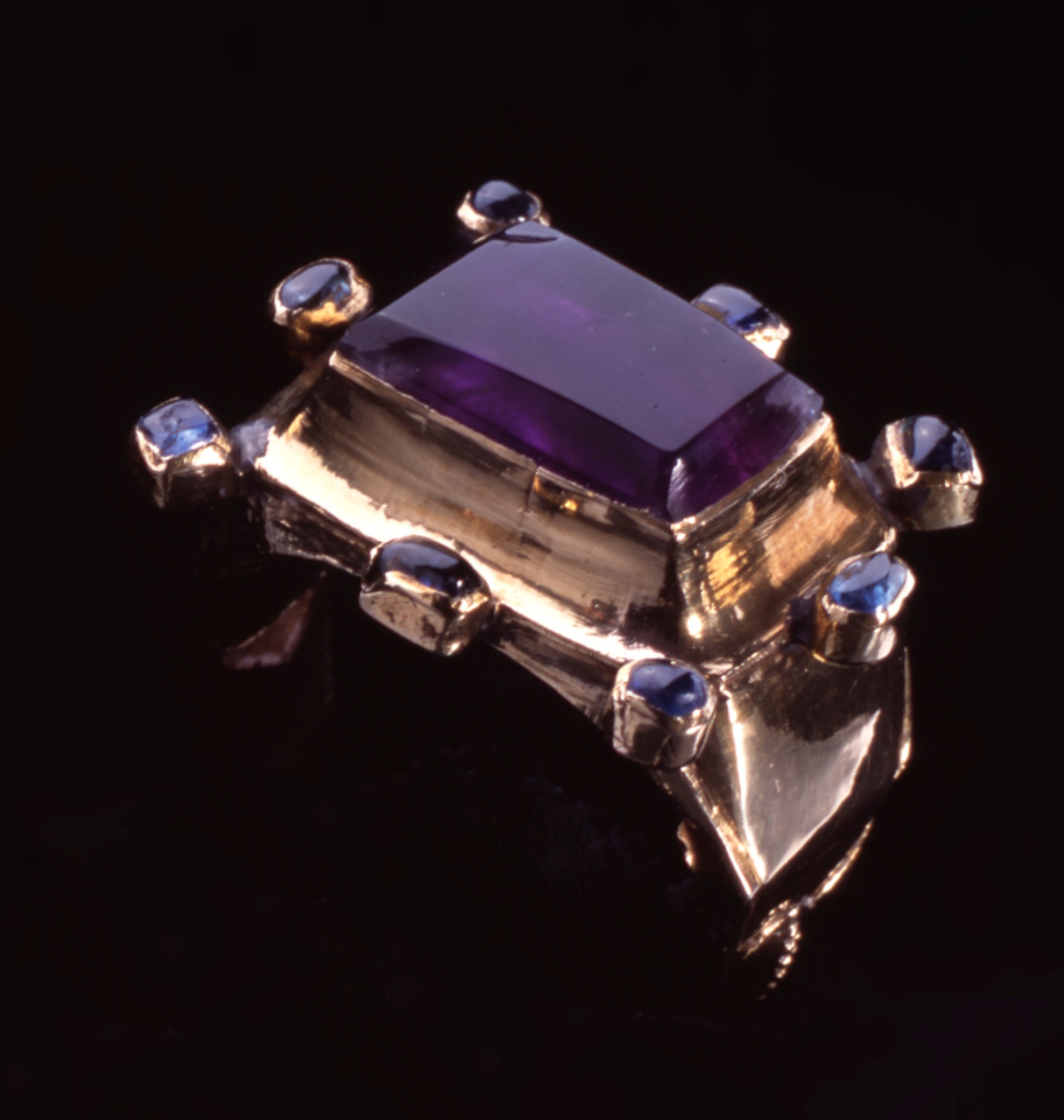 Gold finger ring with a large bezel set with an oblong, table cut amethyst surrounded by eight small sapphires in individual collets (H.1992.1835)