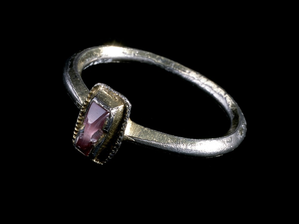 Shiny silver ring on a black background. A small rectangular purple gemstone is set within a raised silver section at the front.